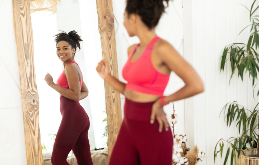 black woman smiling at her body in the mirror