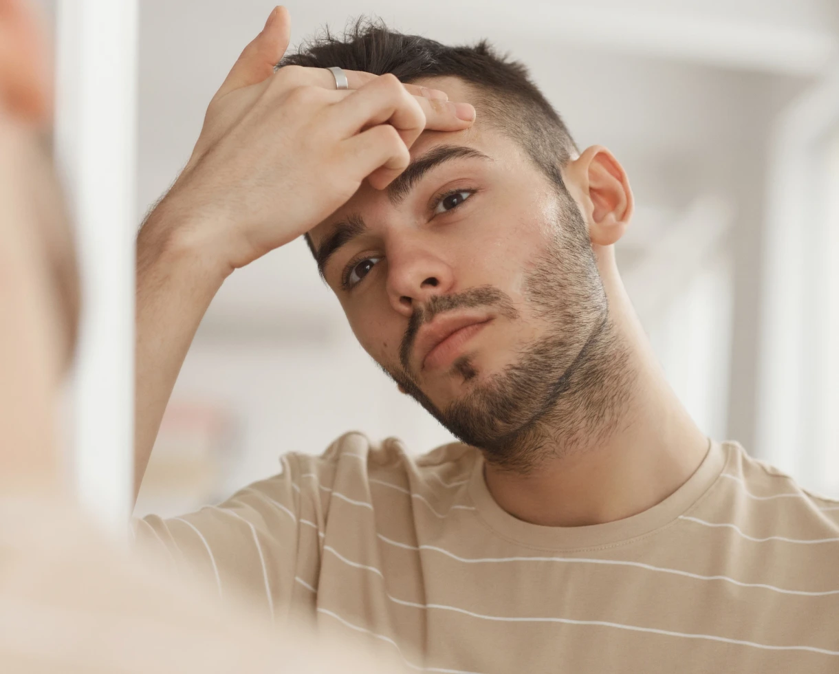 man looking at skin in the mirror and assessing