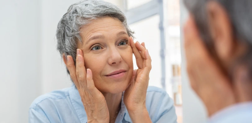 older woman looking at face wrinkles in the mirror